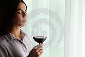 Beautiful young woman with glass of luxury red wine indoors