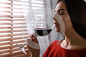 Beautiful young woman with glass of luxury red wine indoors