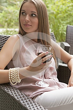 Beautiful young woman with glass of red wine sitting on chair outdoors