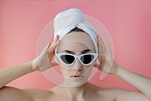 Beautiful young woman in glasses with a towel on her head after bath on pink background