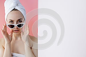 Beautiful young woman in glasses with a towel on her head after bath on pink background