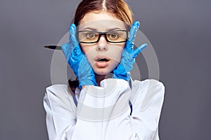 Beautiful young woman in a glove and in medical clothes on a dark gray background holds a pen, doctor, medicine