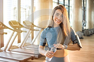 Beautiful young woman going to drink water from plastic bottle after workout in gym.