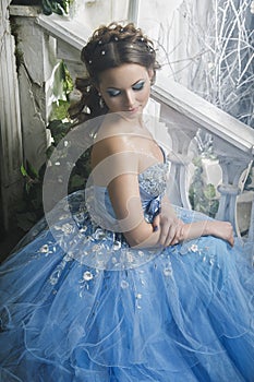 Beautiful young woman in gorgeous blue long dress like Cinderella with perfect make-up and hair style