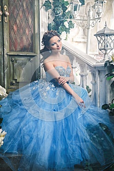 Beautiful young woman in gorgeous blue long dress like Cinderella with perfect make-up and hair style