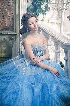 Beautiful young woman in gorgeous blue long dress like Cinderella with perfect make-up and hair style