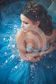 Beautiful young woman in gorgeous blue long dress like Cinderella with perfect make-up and hair style