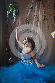 Beautiful young woman in gorgeous blue long dress like Cinderella with perfect make-up and hair style