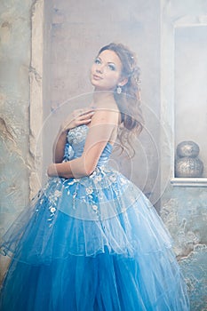 Beautiful young woman in gorgeous blue long dress like Cinderella with perfect make-up and hair style