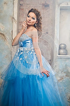 Beautiful young woman in gorgeous blue long dress like Cinderella with perfect make-up and hair style