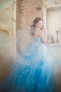 Beautiful young woman in gorgeous blue long dress like Cinderella with perfect make-up and hair style