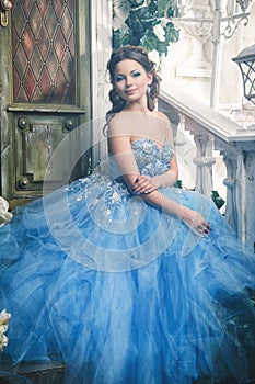 Beautiful young woman in gorgeous blue long dress like Cinderella with perfect make-up and hair style