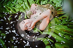 A beautiful young woman in a green dress lies on a train among the white petals of an apple tree