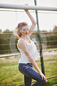 Beautiful young woman on a green football field. Girl standing at football gate, dressed in blue jeans, a white t-shirt