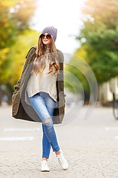 Beautiful young woman in green knitted cardigan with a hood walking in autumn park. Autumn fashin concept.