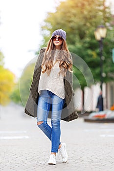 Beautiful young woman in green knitted cardigan with a hood walking in autumn park. Autumn fashin concept.