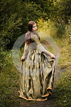 Beautiful young woman in a green rococo dress, walk through the park. A model with clean skin.