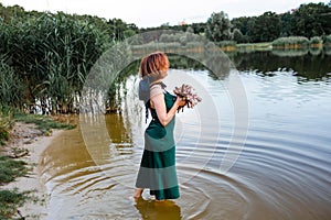 Beautiful young woman in green silk evening dress holding water lily flower outdoors.