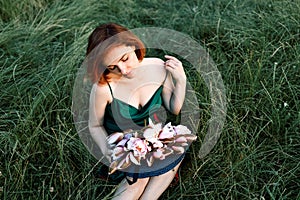 Beautiful young woman in green silk evening dress holding water lily flower outdoors.
