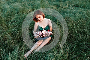 Beautiful young woman in green silk evening dress holding water lily flower outdoors.