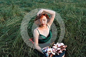 Beautiful young woman in green silk evening dress holding water lily flower outdoors.