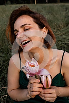 Beautiful young woman in green silk evening dress holding water lily flower outdoors.