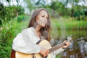 Beautiful young woman with guitar on the river