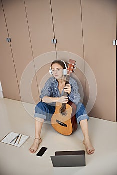 Beautiful young woman with guitar sitting on the floor