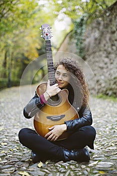 Beautiful young woman with a guitar sitting on the forest.