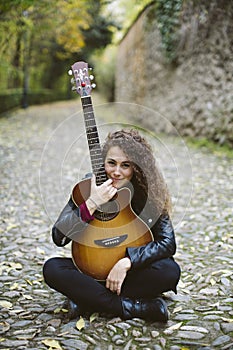 Beautiful young woman with a guitar sitting on the forest.