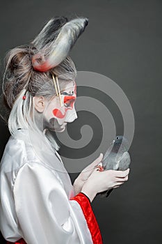 Beautiful young woman in Halloween makeup and costume holding bird on black background