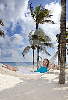 Beautiful young woman in a hammock on the beach on background of palm trees and the sea