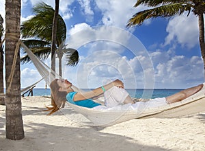 Beautiful young woman in a hammock on the beach on background of palm trees and the sea