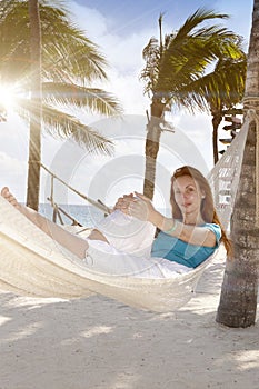 Beautiful young woman in a hammock on the beach on background of palm trees and the sea