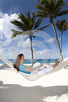 Beautiful young woman in a hammock on the beach on background of palm trees and the sea