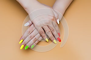 Beautiful young woman hands with summer different color nail on pastel peach background. Stylish trendy female multicolored