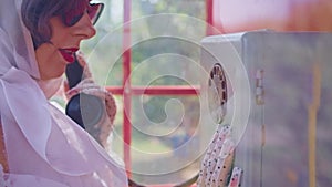 beautiful young woman happily talking on the phone in a red telephone booth in English style. girl in a white dress and