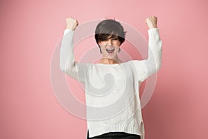 Beautiful young woman happy and excited expressing winning gesture. Successful pretty girl celebrating victory, triumphant, studio