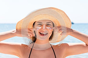 Beautiful young woman in hat is applying sunblock under her eyes and on her nose like Indian. Sun protection concept