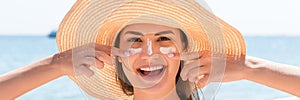 Beautiful young woman in hat is applying sunblock under her eyes and on her nose like Indian. Sun protection concept