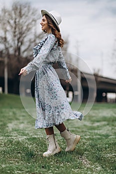 beautiful young woman in a hat and a blue dress is dancing in a field of wildflowers. Spring