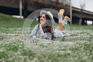 beautiful young woman in a hat and a blue dress lies on a field of wildflowers. Spring