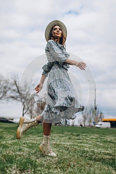 a beautiful young woman in a hat and a blue dress runs through a field of wildflowers. Spring