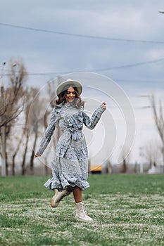 a beautiful young woman in a hat and a blue dress runs through a field of wildflowers. Spring