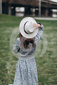 beautiful young woman in a hat and dress on the background of a field with flowers