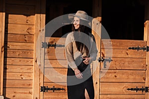 Beautiful young woman in a hat near wooden building outdoors on autumn sunny day
