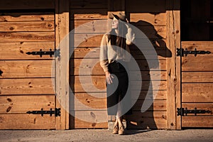 Beautiful young woman in a hat near wooden building outdoors on autumn sunny day