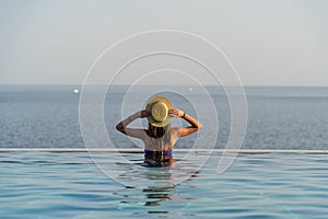 Beautiful young woman with a hat is relaxing in an infinity pool with a breathtaking view