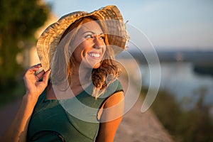 Beautiful young woman with a hat smiling at the sunset