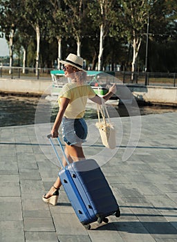 Beautiful young woman in hat with suitcase and wine glass waiting a ship for summer trip.